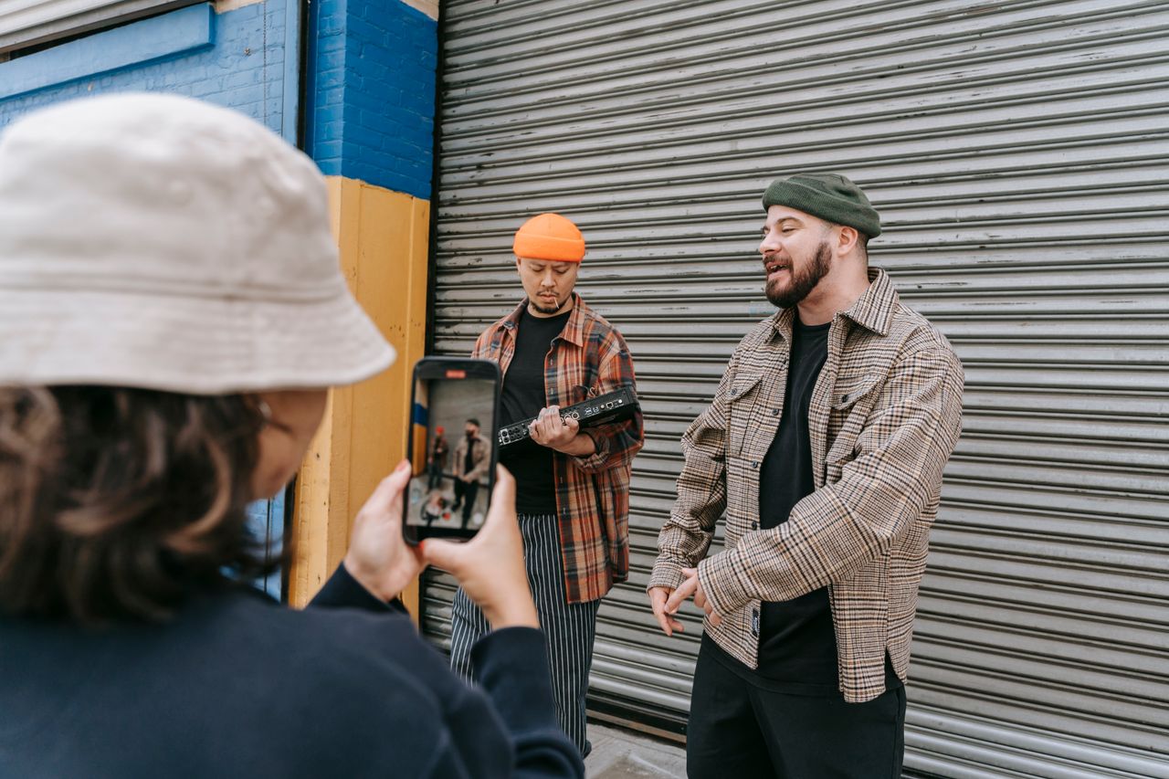 Musicians perform in an urban setting while being filmed by a mobile device.